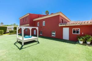 une cour avec une balançoire blanche devant une maison rouge dans l'établissement Ohana Luxury Villa with Heated Pool, à Malaga