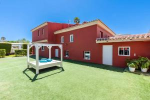 a yard with a white swing in front of a red house at Ohana Luxury Villa with Heated Pool in Málaga