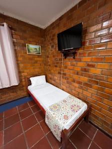 a small room with a bed and a tv on a brick wall at Pousada Dona Felicidade Carneiros in Tamandaré