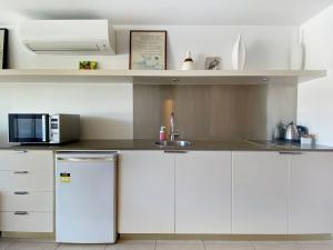 eine weiße Küche mit einer Spüle und einer Mikrowelle in der Unterkunft Blue on Blue Superior Studio Room 1221 in Nelly Bay