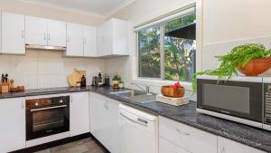 a kitchen with white cabinets and a large window at Kangaroo Cottage in Currarong