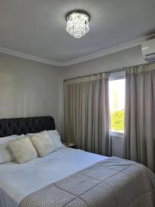 a bedroom with a bed with a chandelier and a window at Aconchegante Apartamento decorado e mobiliado in Cascavel