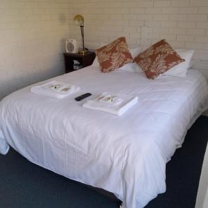 a white bed with two towels and a remote control on it at The Frontier Motel in Dorrigo