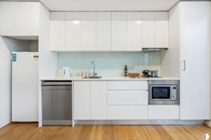 a kitchen with white cabinets and a refrigerator at Central, modern 1 bedroom with air-con & balcony in Sydney