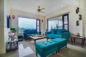 a living room with blue furniture and large windows at SaffronStays Summer Estate in Kasauli