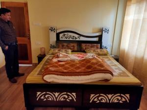 a man standing next to a bed in a room at Conifers Homestay in Shimla