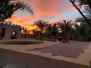 un homme prend une photo du coucher du soleil dans l'établissement Al Kahina Gardens, Retreat and Resort, à Siwa
