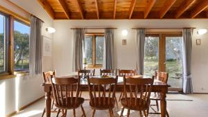 uma sala de jantar com mesa, cadeiras e janelas em Wrens View em Dinner Plain