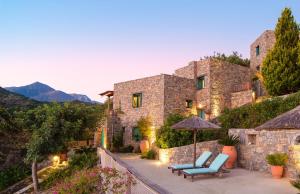 莫克羅斯的住宿－Villa Ilios，石头房子,配有两把蓝色椅子和一把遮阳伞