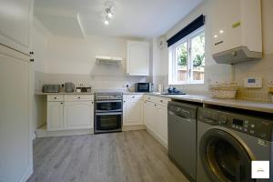 cocina con armarios blancos, lavadora y secadora en Camberley Spacious and Comfy 3 Bedroom Home, Next to Frimley Hospital with Parking, en Frimley