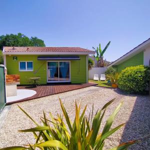 ein grünes Haus mit einer Holzterrasse davor in der Unterkunft Gîte avec piscine jacuzzi espace bien-être partagés entre Bordeaux et Lacanau océan in Brach