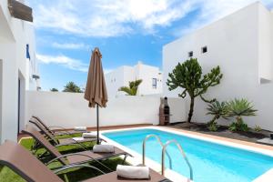 a pool in the backyard of a villa with chairs and an umbrella at Luxury 3-bedroom villa with private pool in Marina Rubicon, Playa Blanca, Lanzarote in Playa Blanca
