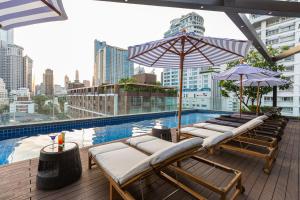 Hotel Icon Bangkok Sukhumvit 2 في بانكوك: مسبح على السطح مع كراسي جلوس ومظلات على مبنى