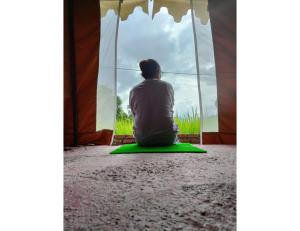 a person sitting on the floor looking out the window at Sumeru Camp,Barkot in Barkot