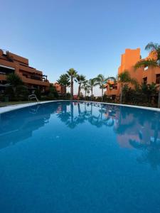uma grande piscina azul com palmeiras e edifícios em Jardines de Nueva Galera em Estepona