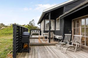 a black house with chairs and a grill on a deck at Summerhouse At The Beach in Rørvig