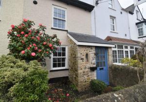 a house with a blue door and a bush with roses at Bluebell Cottage - Seaton in Seaton