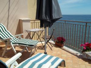 a balcony with chairs and an umbrella and the ocean at Mare e Monti in Giardini Naxos