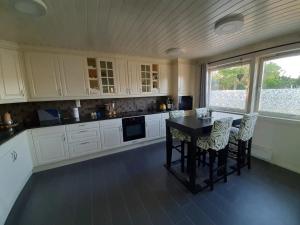 cocina con armarios blancos, mesa y sillas en Cosy family home with pool en Grimstad