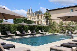 a pool with chairs and umbrellas in front of a building at Château Hôtel Grand Barrail in Saint-Émilion