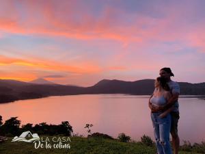 a pregnant woman standing next to a lake with a sunset at Vista al Volcán Tenorio y Montaña in San Rafael