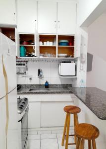 een keuken met witte kasten en 2 krukken bij Apartamento bem localizado. in Praia Grande