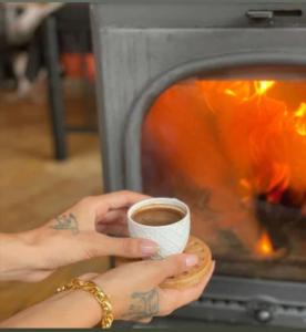 a person holding a cup of coffee in front of a fireplace at İstanbuldere Glamping in Sapanca