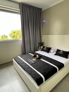a bedroom with a bed with black and white sheets and a window at Motel Hofim in Bat Yam