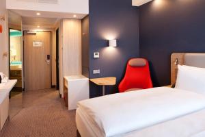 a hotel room with a bed and a red chair at Holiday Inn Express Munich - Olching, an IHG Hotel in Olching