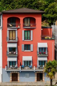 ein rotes Gebäude mit Balkonen und einer Palme in der Unterkunft 76 The Lake House - Lugano in Melide