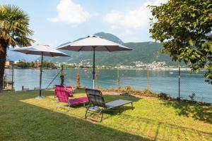 zwei Stühle und Sonnenschirme auf dem Gras in der Nähe des Wassers in der Unterkunft 76 The Lake House - Lugano in Melide