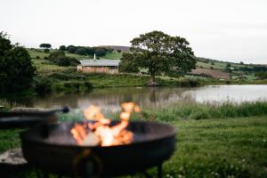 a barbecue grill with a fire in front of a lake at Under the Oak Glamping in Caerphilly