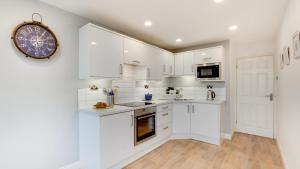 a kitchen with white cabinets and a clock on the wall at Limeslade Court in The Mumbles