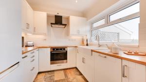 eine Küche mit weißen Schränken, einem Waschbecken und einem Fenster in der Unterkunft Delfryn Cottage in The Mumbles