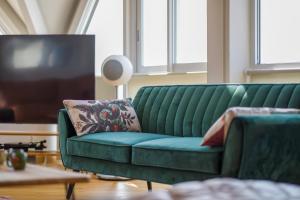 um sofá verde numa sala de estar com uma televisão em Le poséidon, gîte EXCEPTIONNEL face à la mer avec spa, terrasse, 4 chambres UN VRAI COUP DE COEUR em Fécamp