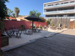 eine Terrasse mit Tischen, Stühlen und einem Sonnenschirm in der Unterkunft Hôtel Les Mimosas in Argelès-sur-Mer