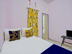 a bedroom with a white bed with yellow and blue pillows at SPOT ON 92564 Kemangi Asri Kost in Banyuwangi
