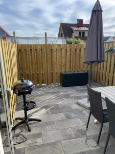 a patio with a grill and an umbrella and a fence at Kaptenhuset Skrea strand in Falkenberg