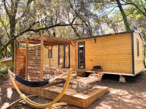 a log cabin with a hammock and chairs in front of it at Camping Sunêlia la Clémentine in Cendras