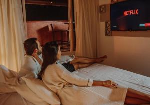 a man and woman sitting on a bed looking out a window at Hotel Ponta Verde Praia do Francês in Praia do Frances