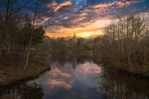 a sunset over a pond with clouds in the water at Unwind@37 Lodge in Felton