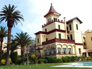 a large house with palm trees in front of it at Hotel Hostal del Sol in Sant Feliu de Guíxols