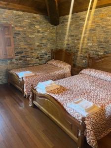 2 aparte bedden in een kamer met een bakstenen muur bij Habitaciones Frade in O Cebrero