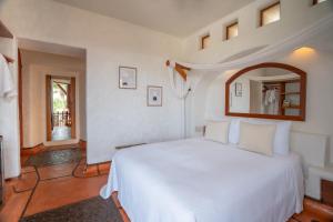 um quarto com uma cama branca e um espelho em La Villa Luz (sólo adultos) em Zihuatanejo