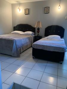 a bedroom with two beds and a white tiled floor at Derick's Inn in Piarco