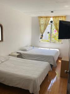 two beds in a room with a television and a window at Casa Verde Hostal in Tlazcalancingo