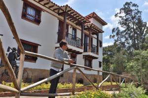 un hombre parado en una barandilla frente a una casa en Casa El Retiro - Villa de Leyva, en Villa de Leyva