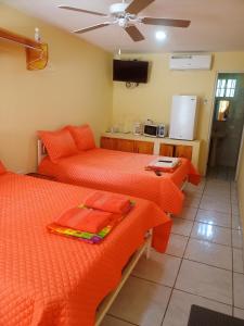 Habitación con 2 camas con sábanas de color naranja y cocina. en Cabañas El Valle, en Antón