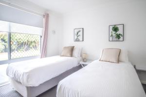two beds in a white room with a window at Bokarina Seaside Escape - Only steps to the Beach in Kawana Waters