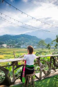 a woman sitting on a fence looking out over a field at Homestay view núi cực đẹp in Cham Ta Lao